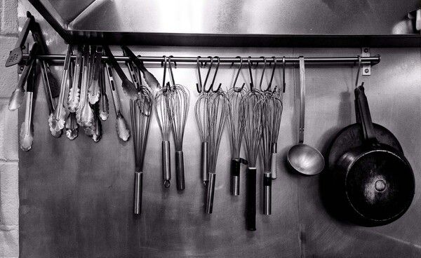 Utensilios de cocina colgados de una barra en una cocina profesional, en blanco y negro